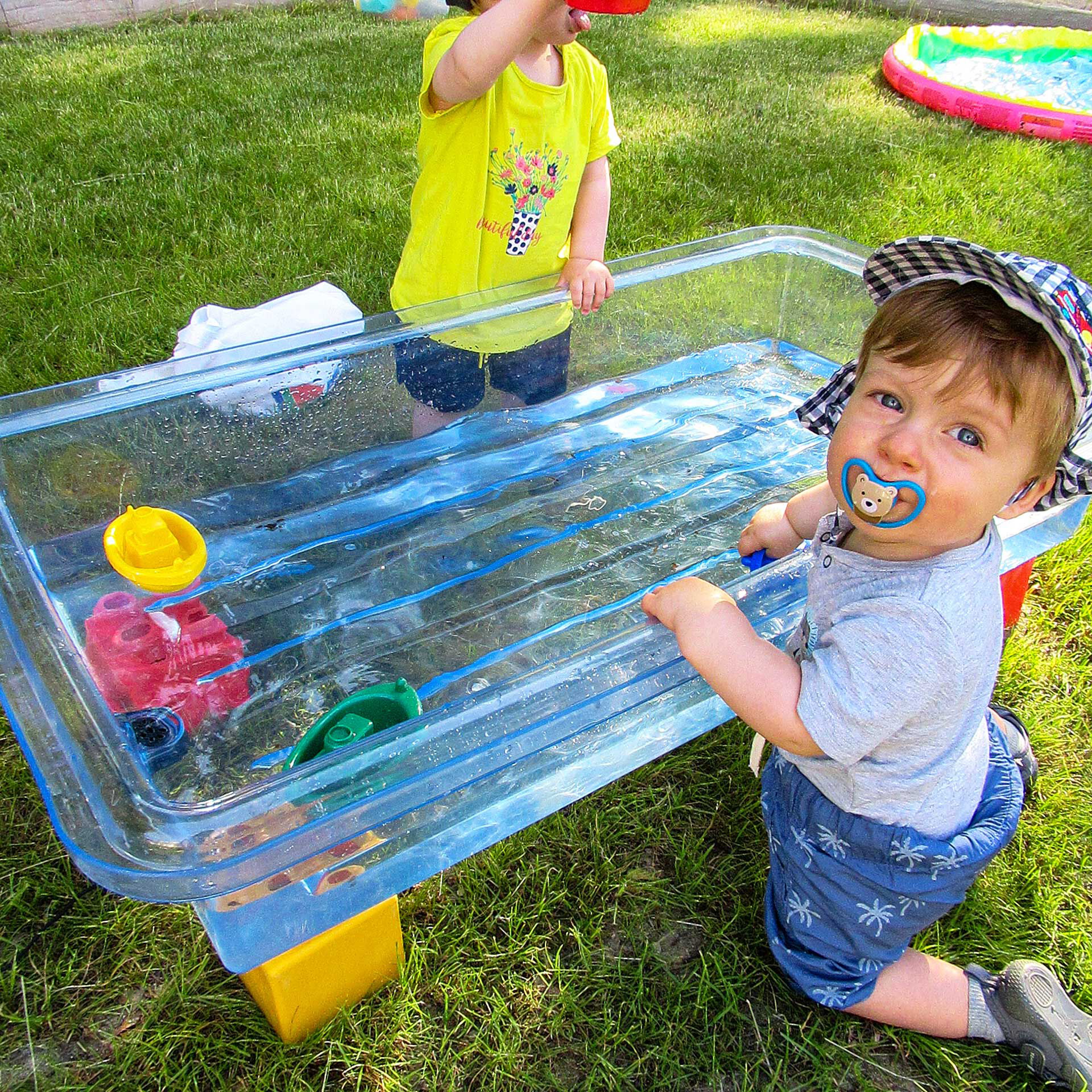 Zwei Kleinkinder spielen mit Spielzeug in einer großen Plastikwanne mit Wasser.