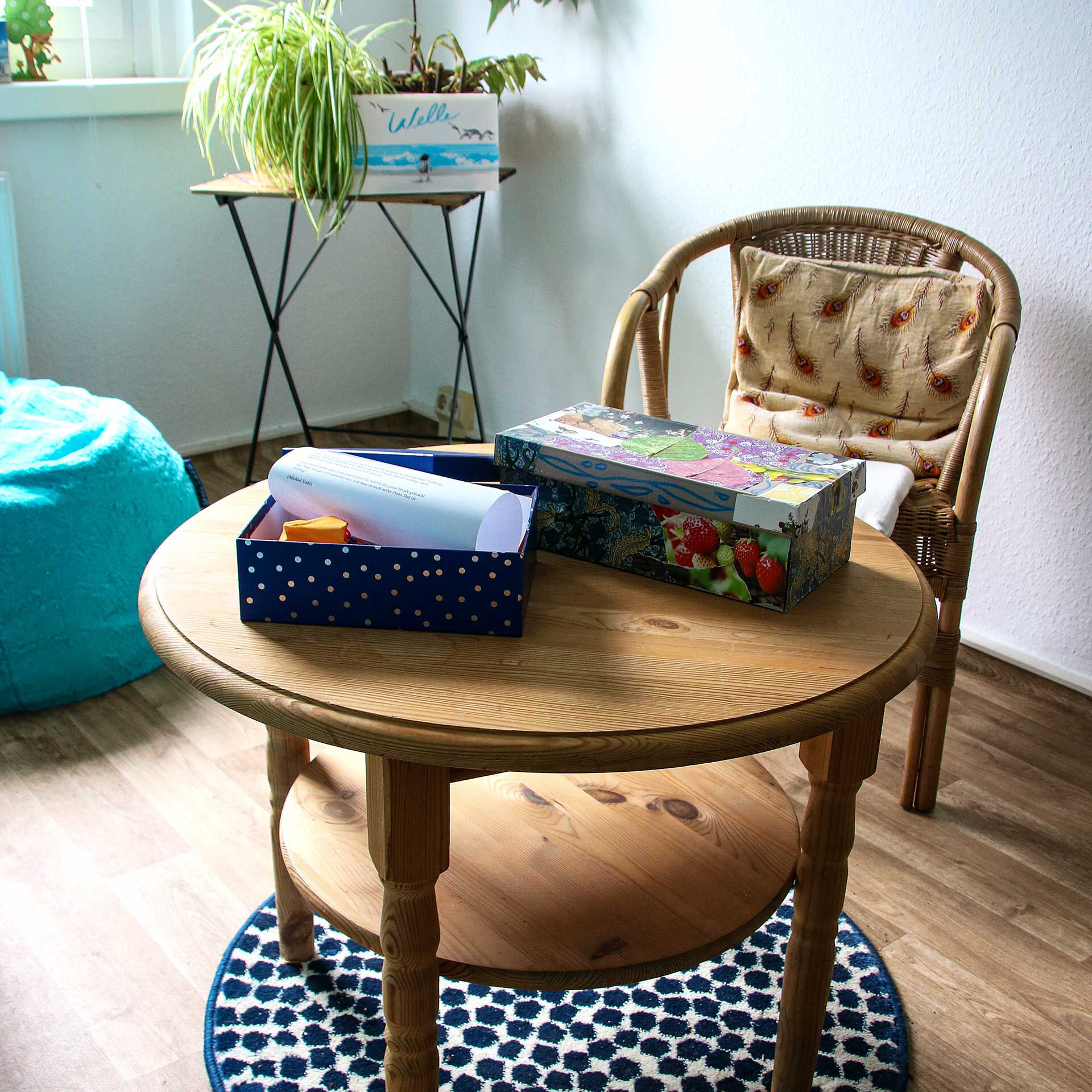 Ein runder Holztisch mit einem Stuhl auf dem eine Box mit Therapieansätzen liegt.