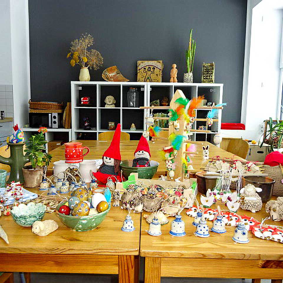 Beim Ostermarkt im Kreativzentrum werden viele Keramikfiguren, Becher, Tassen und Schüssel zum Verkauf angeboten. Es stehen viele selbstgemachte Ostersachen auf einem großen Holztisch.