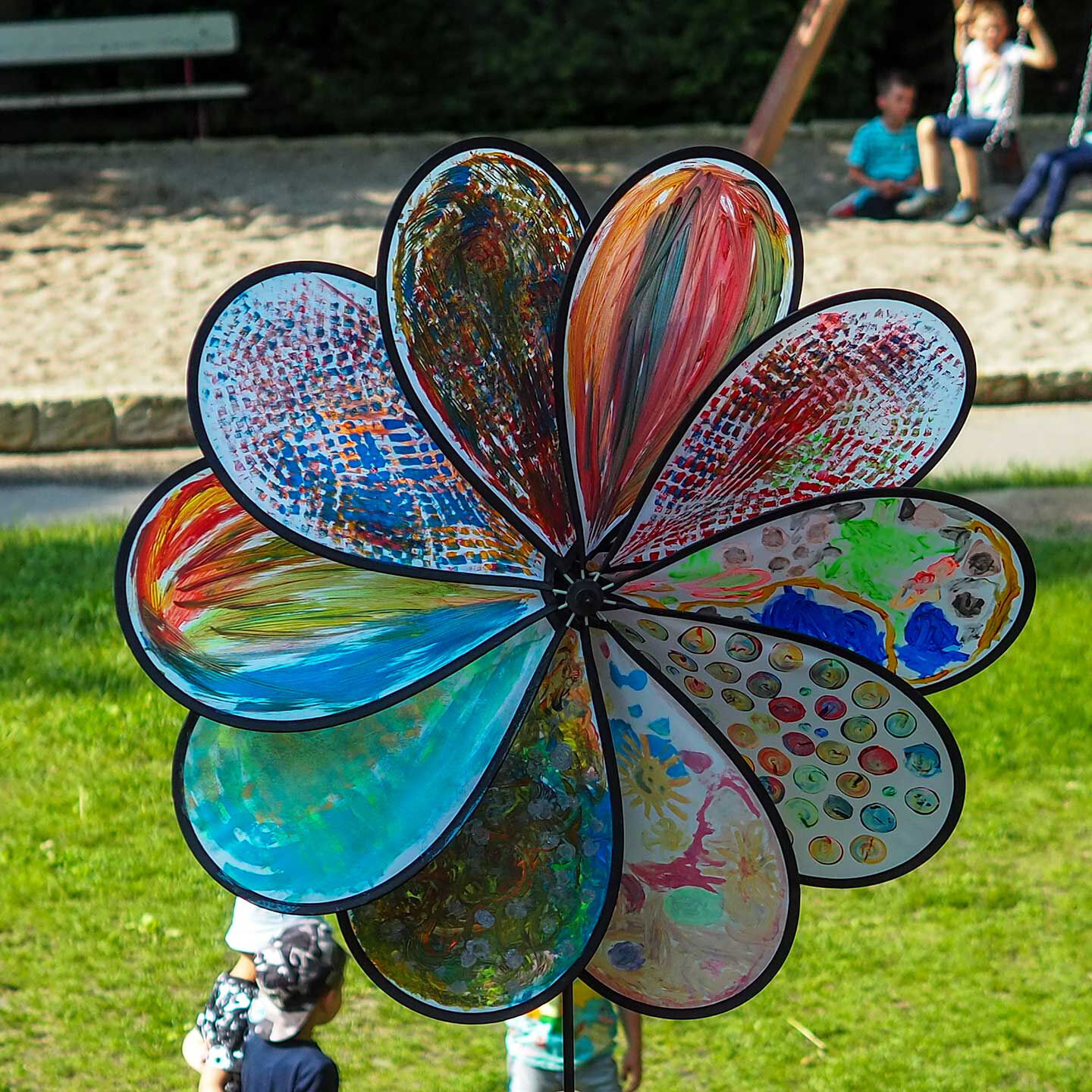 Ein Windrad wurde von Kindern eigenständig mit vielen bunten Farben bemalt und steht auf der Wiese im Außengelände.