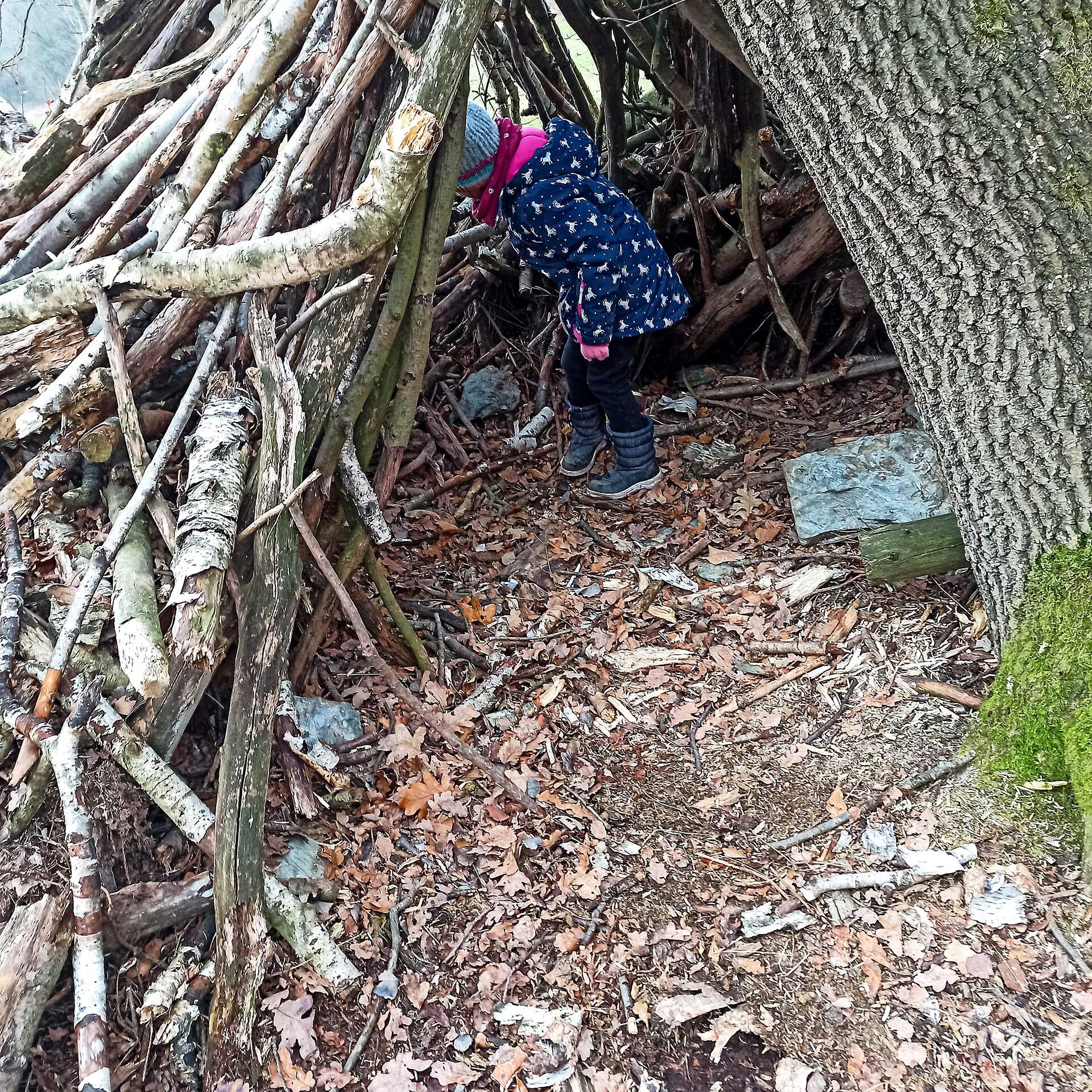 Ein Mädchen spielt in einer Hütte aus Stöcken.