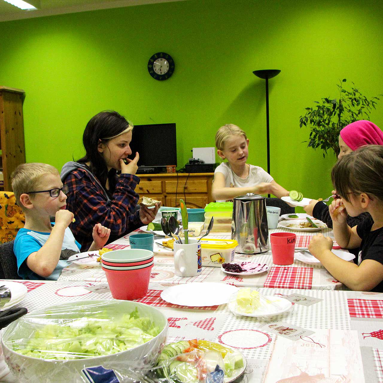 An einem großen Esstisch sitzen fünf Kinder und essen zu Abend. Auf dem Tisch stehen Teller, Schüsseln und es gibt Salat und Suppe.