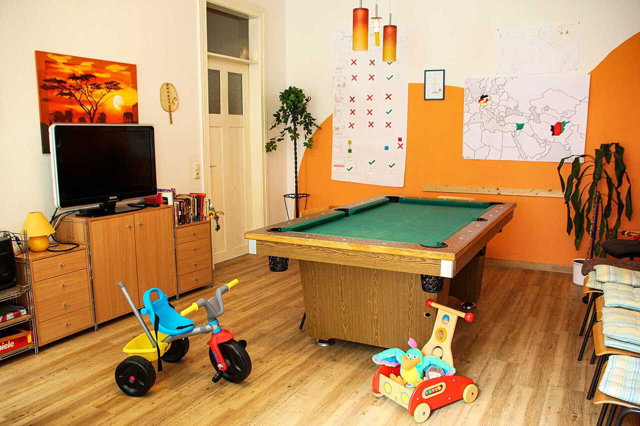 Ein großer Gruppenraum mit einem Billardtisch, TV, Dreirad, Lernlaufwagen und einer Kommode.