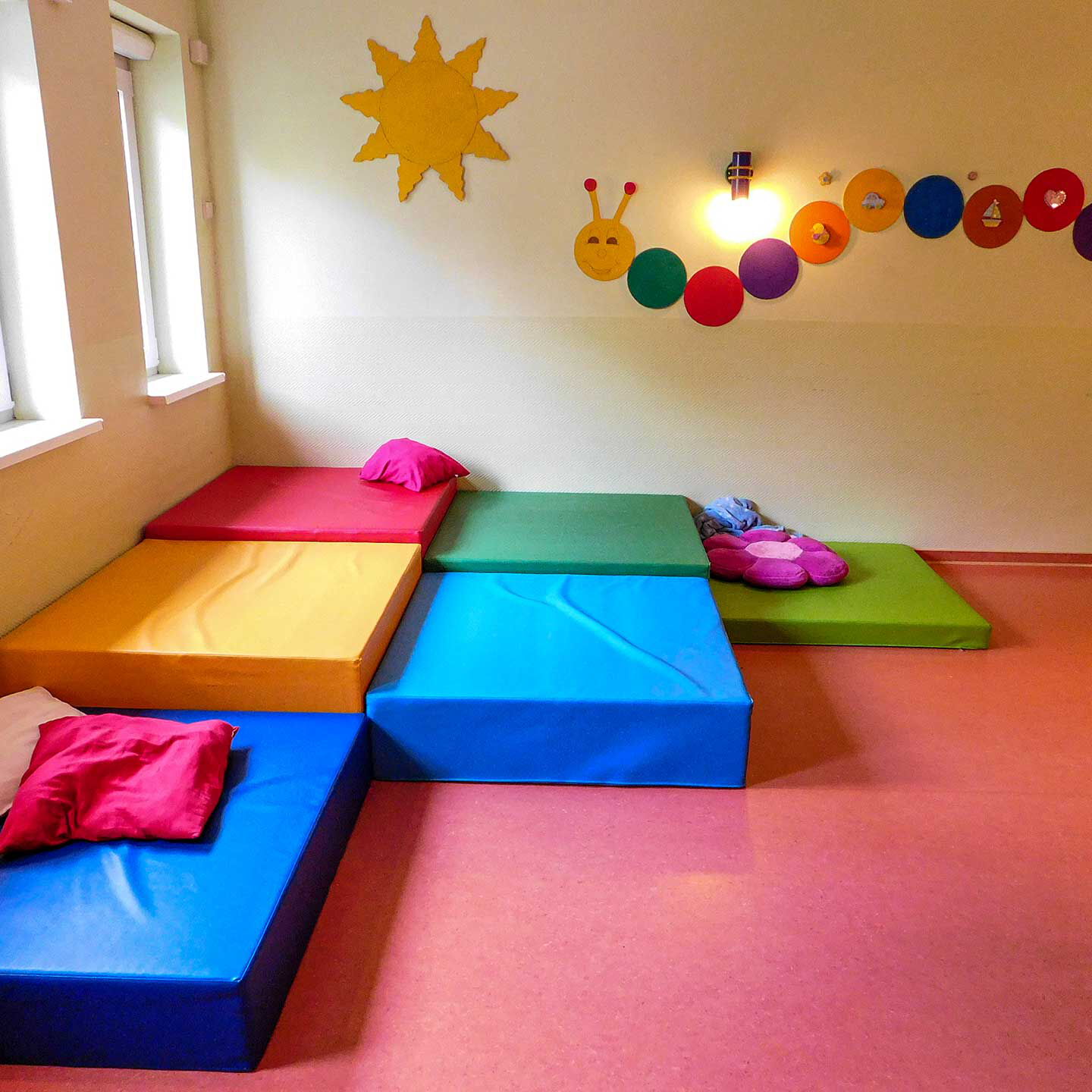 Eine Kuschelecke mit vielen weichen Matratzen und Kissen. An der Wand hängt eine Sonne und Raupe.