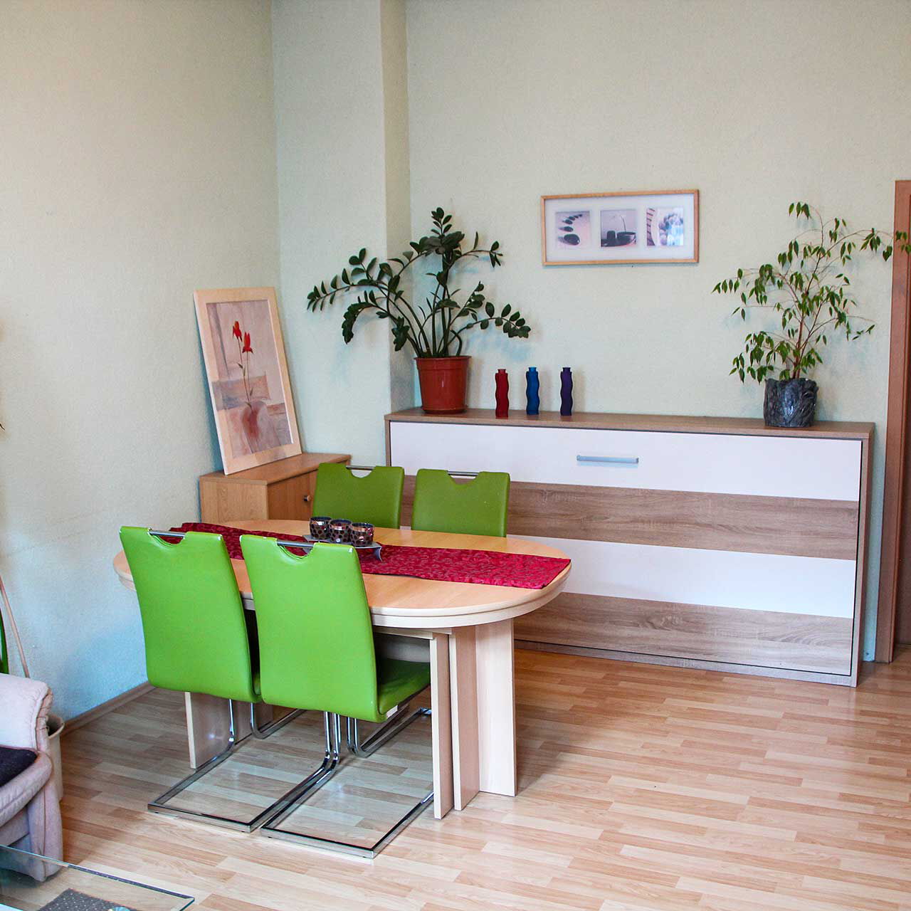 Ein Gruppenzimmer mit Anbauwand, Tisch mit Stühlen und einem Fernseher.