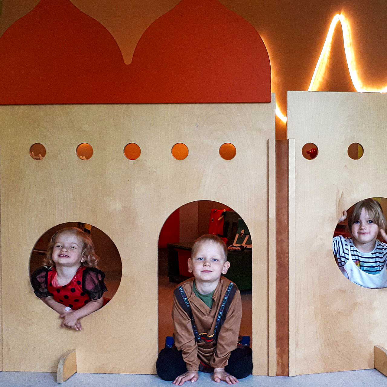Ein Schloss aus verschiedenen Holzplatten in dem drei Kinder sitzen.