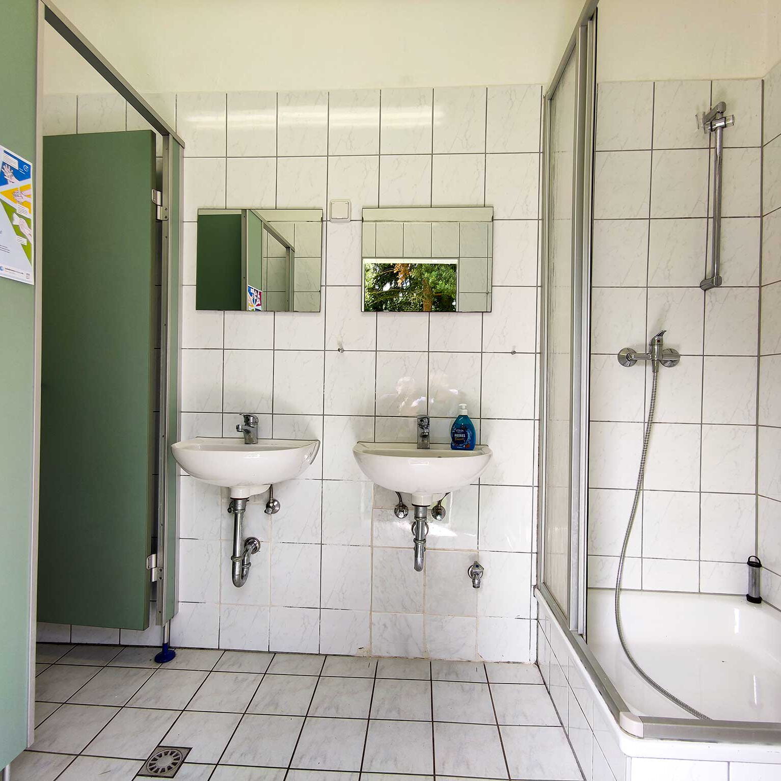 Ein gefliester Raum mit Dusche, WC und zwei Waschbecken.