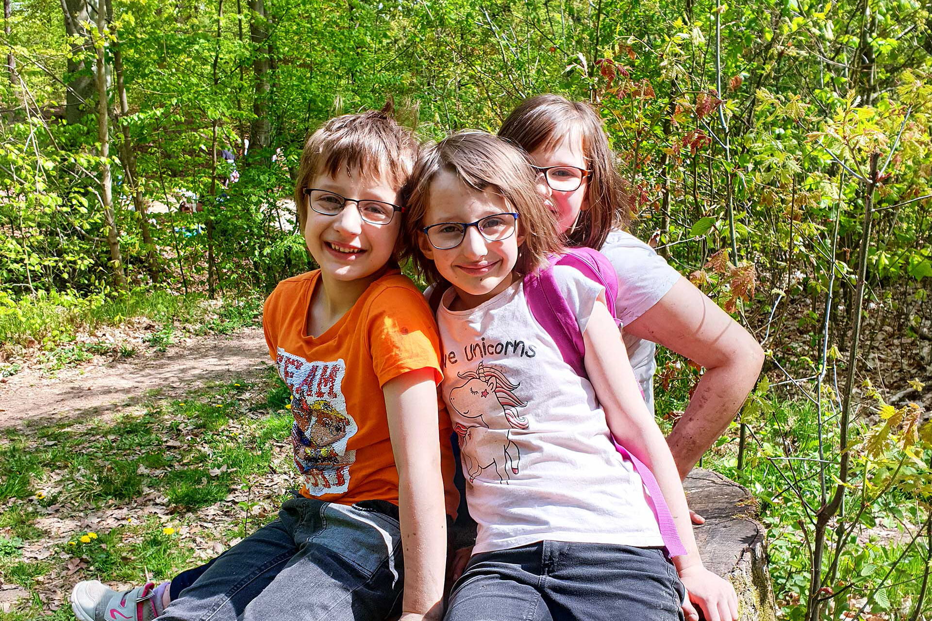 Drei Kinder sitzen auf einem Baumstumpf.