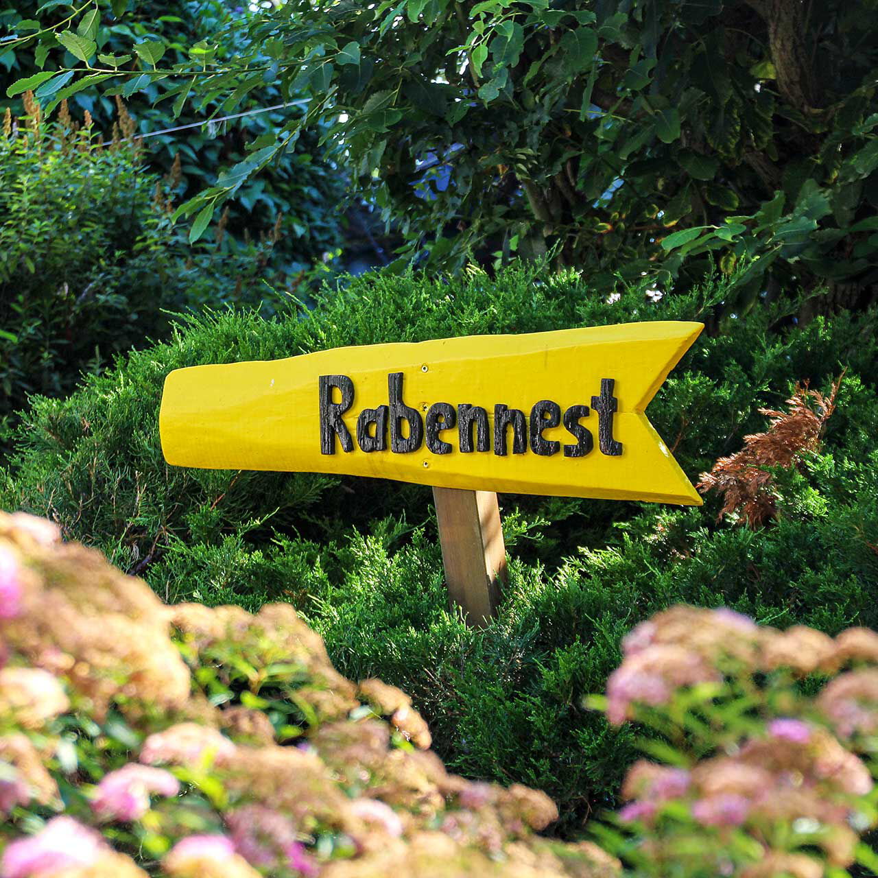 Ein gelber Wegweiser im Garten mit einer schwarzen Aufschrift Rabennest.