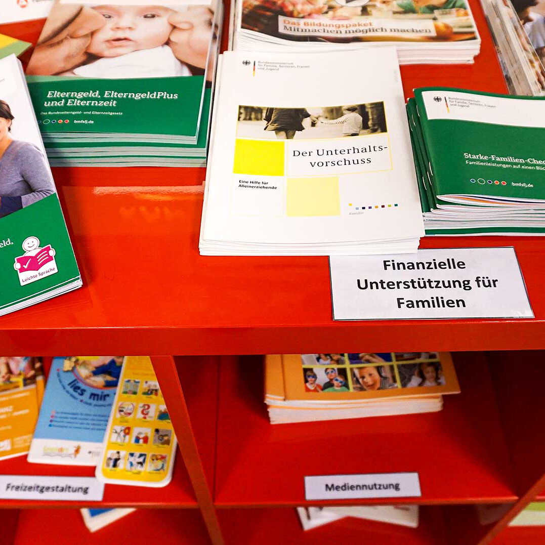 Ein rotes Regal mit mehreren Zeitschriften und Informationsmaterial für Eltern.