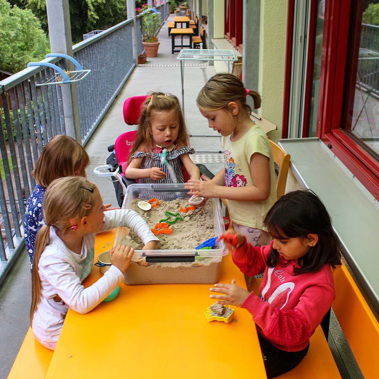 Fünf Kinder spielen in einer mit Sand befüllten großen Box auf der Terrasse der Einrichtung.