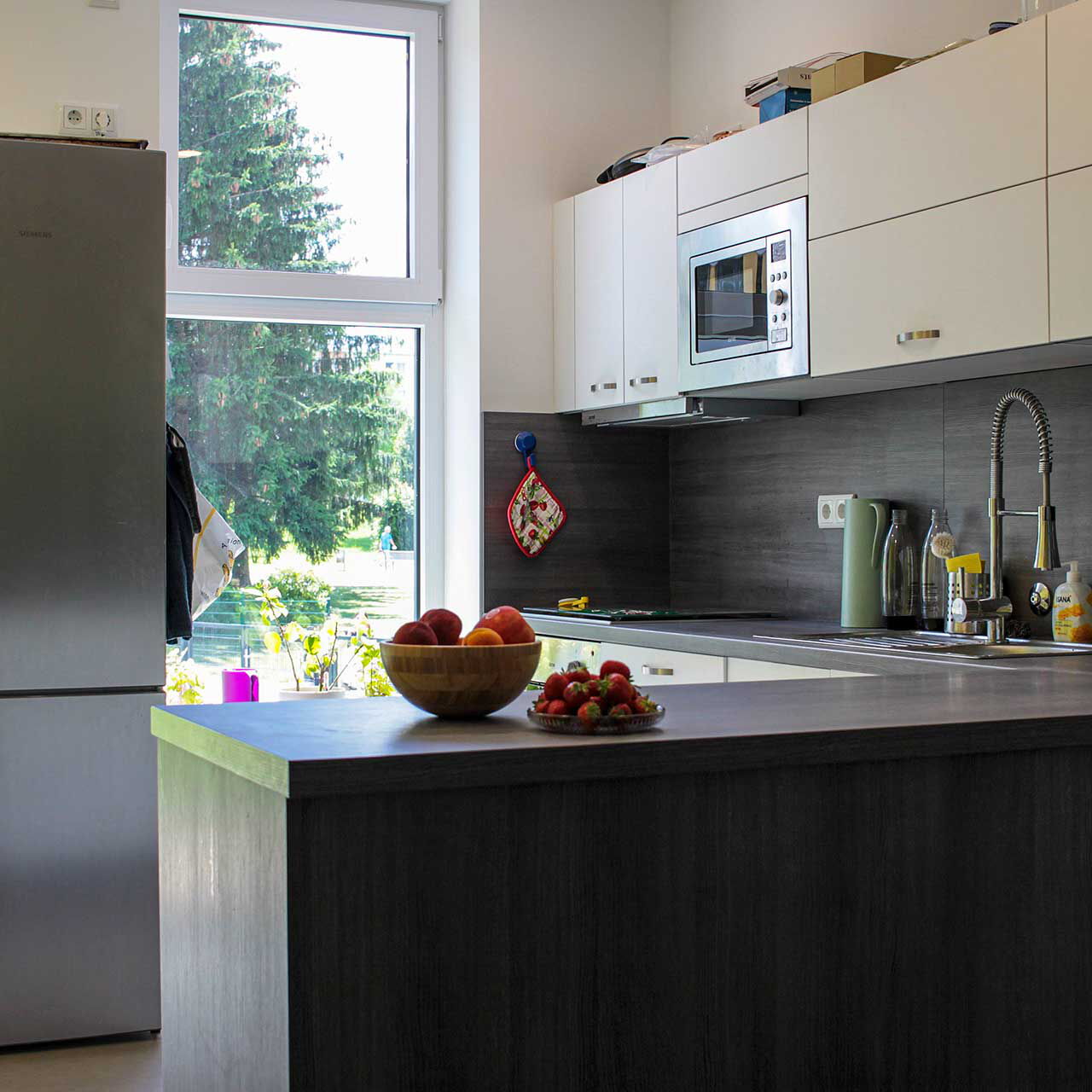 Eine kleine graue Einbauküche mit Mikrowelle, Spüle, Herd und großen Edelstahlkühlschrank.