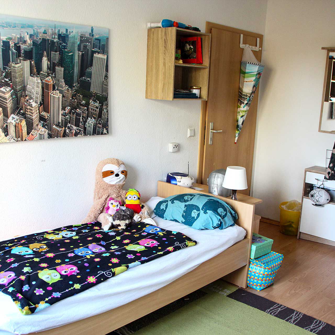Ein Kinderzimmer mit Bett, Garderobe, Wandboard und Wandbild.