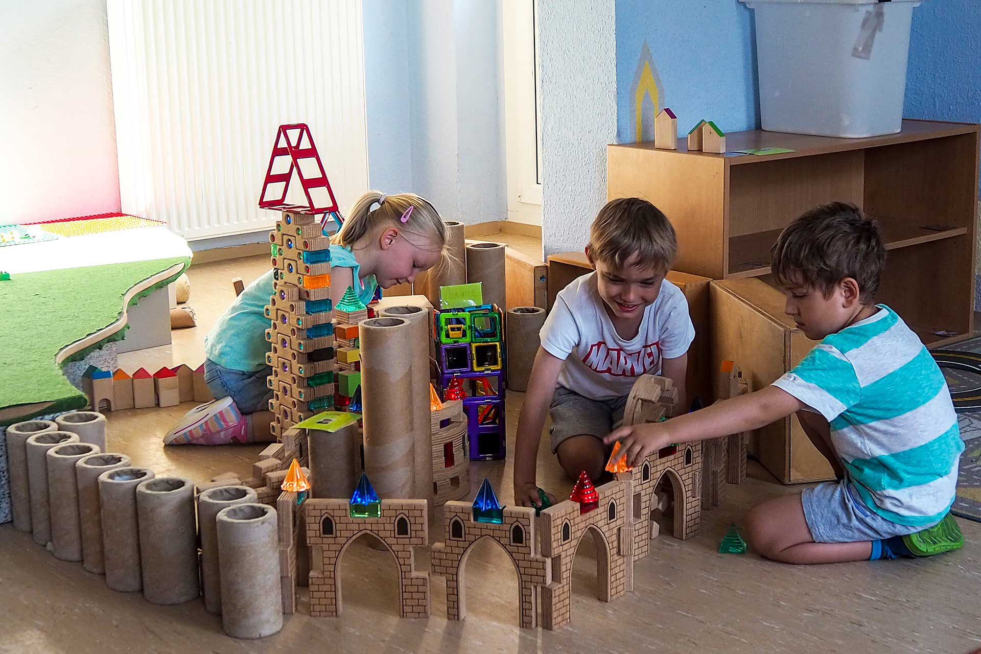 Im Bauzimmer spielen drei Kinder mit Bausteinen und haben viele Türme und Zäune aufgebaut.