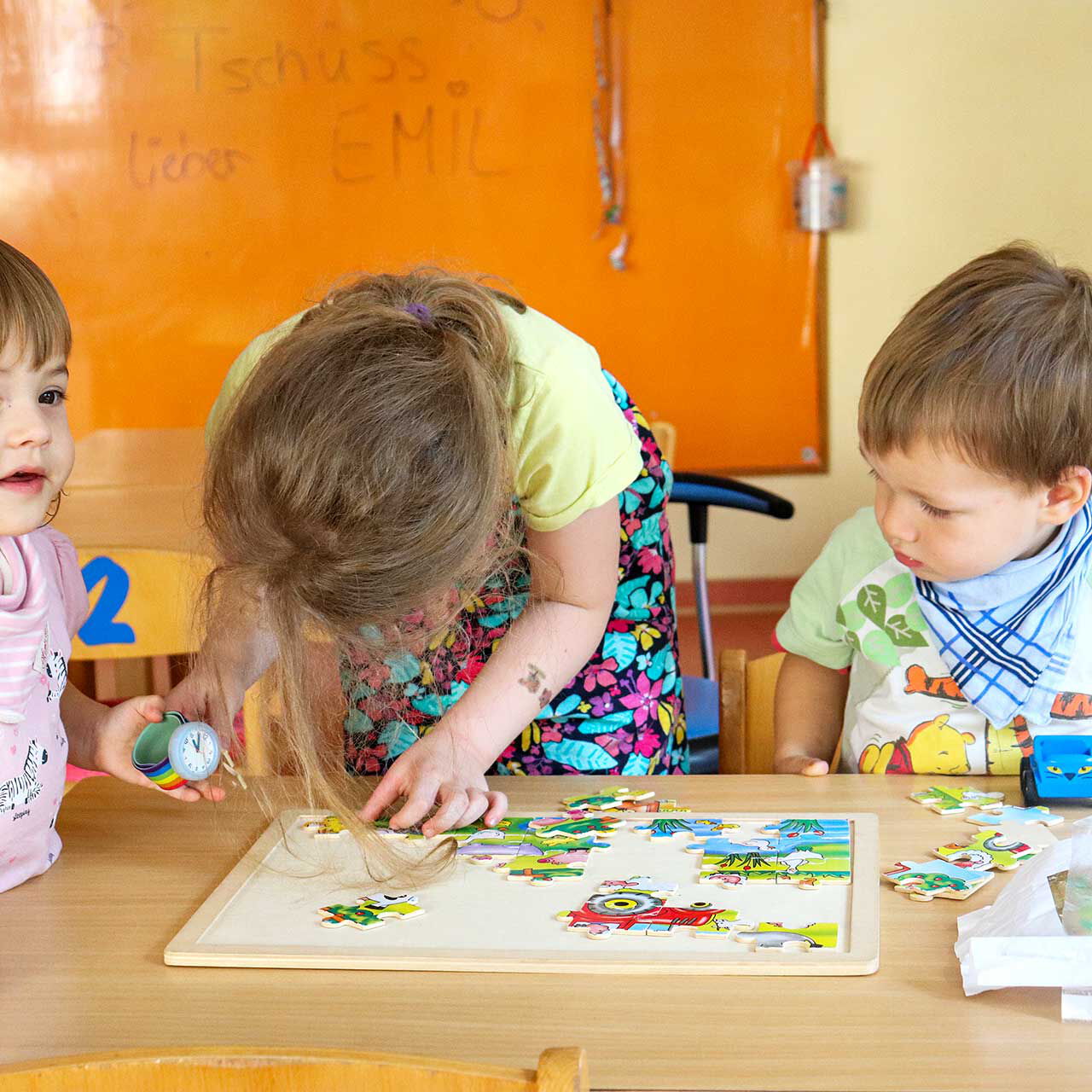 Drei Kleinkinder versuchen sich am Puzzlespiel. Sie sitzen an einem Tisch und versuchen das richtige Bild zu legen.