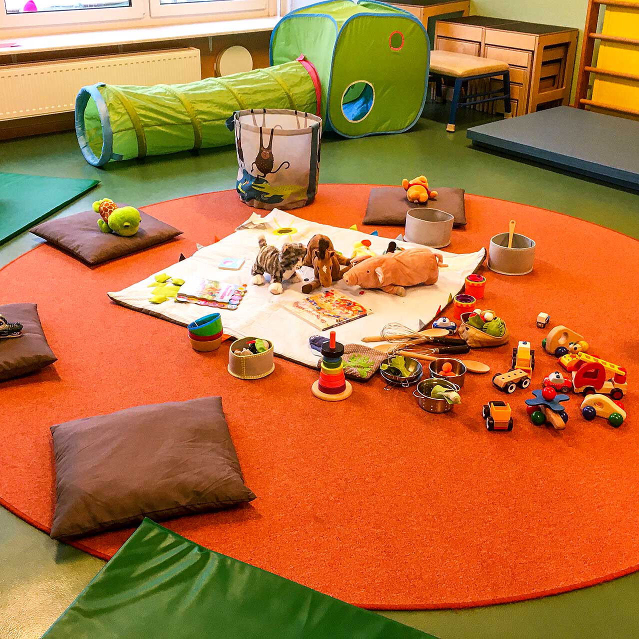 Zur Spielstunde sind auf dem Fußboden im Spielzimmer Decken und Matten mit viel Spielzeug ausgebreitet.