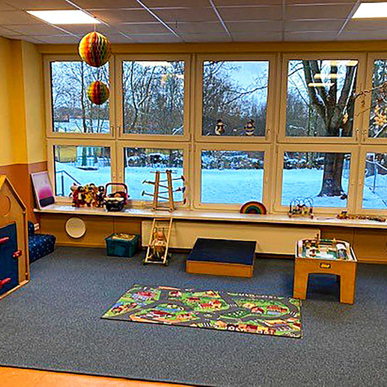 Das Gruppenzimmer im Kleinkindbereich mit einem Spielteppich, Kinderspielküche, Puppenhaus und vielen Kleinkindspielzeug.