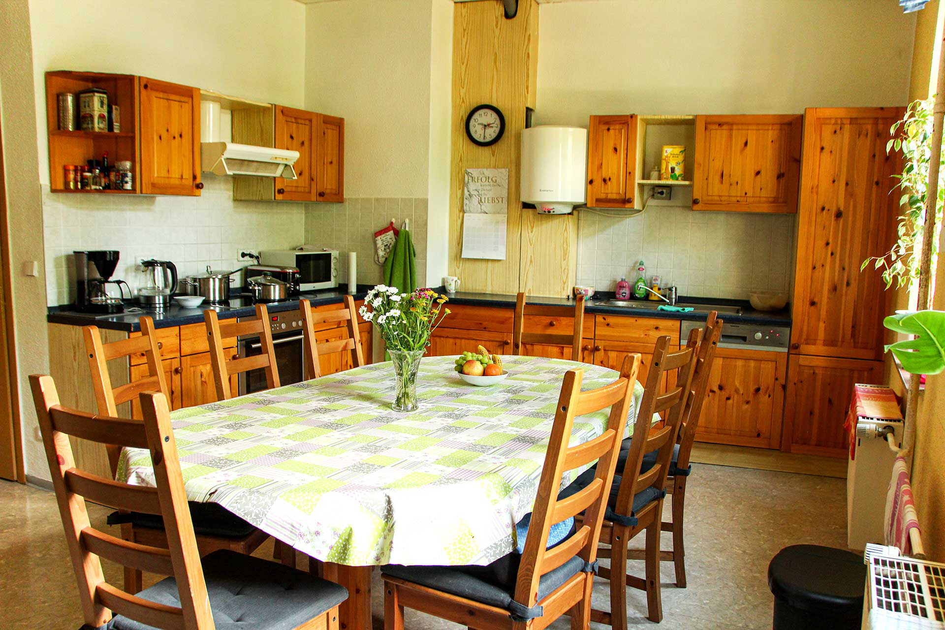 Eine Wohnküche mit einer großen Küchenzeile mit Elektrogeräten und einem Küchentisch mit acht Stühlen.