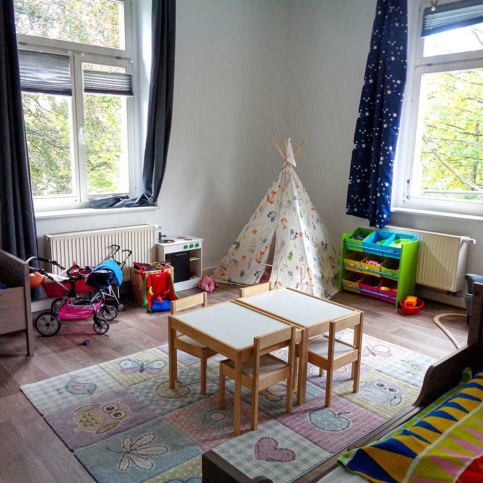 Eine Spielecke in einem Kinderzimmer mit Regal, Tipi, Kinderküche, Puppenwagen und zwei Kinderbetten.