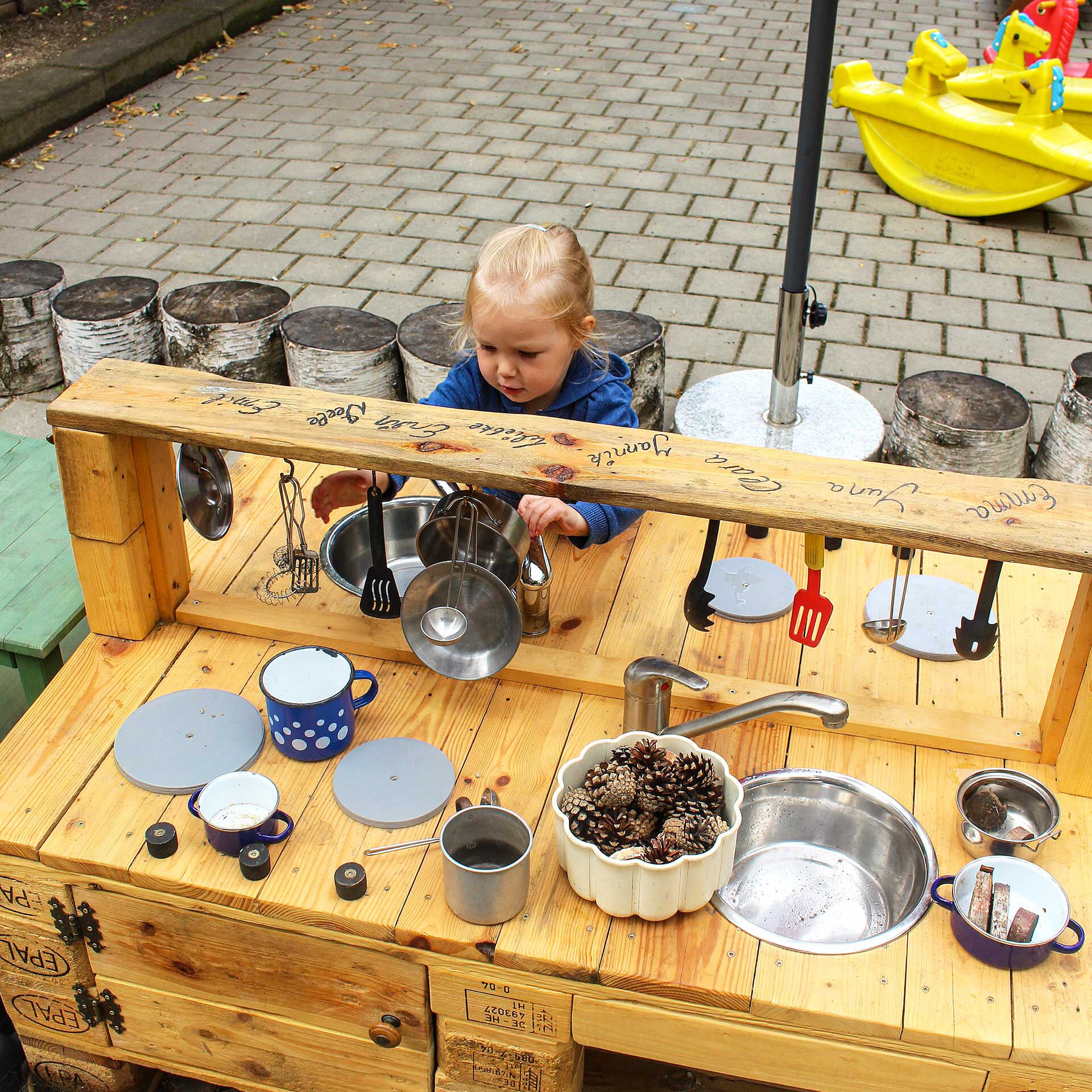 Eine selbstgebaute Spielküche aus Holzpaletten. Ein Mädchen spielt mit Geschirr in der Spüle.