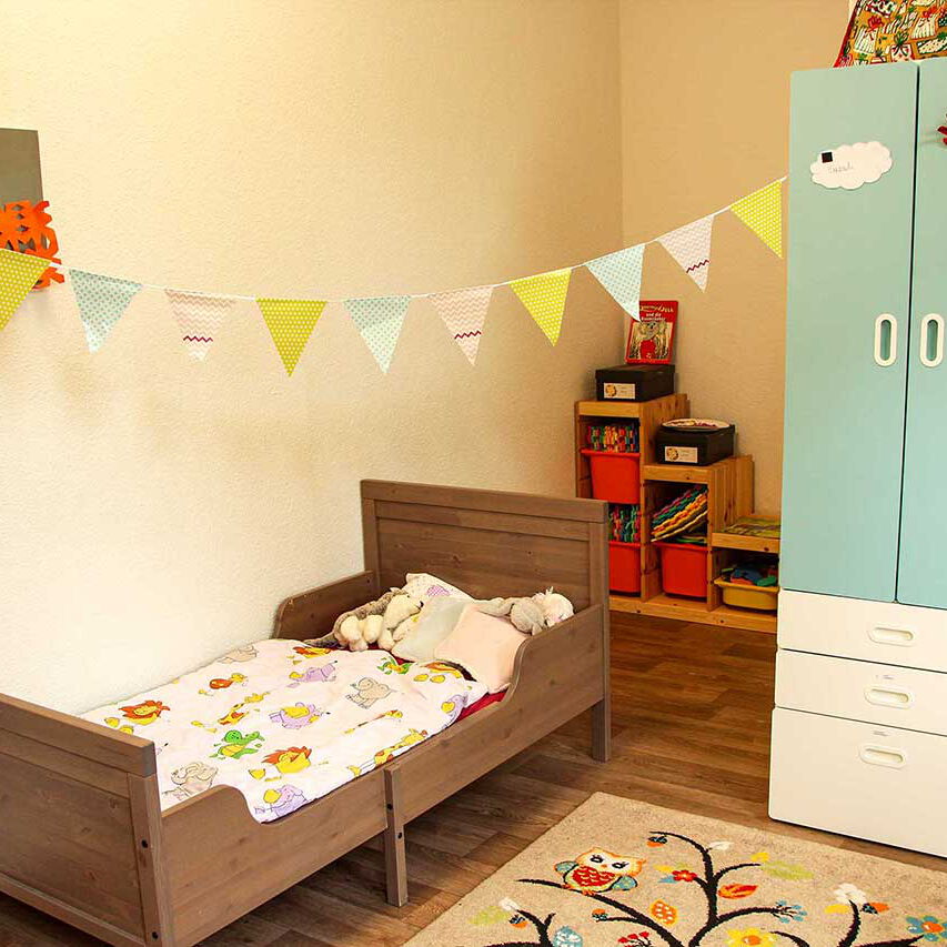 Ein Kinderzimmer mit Kinderbett, Kleiderschrank und einer Spielecke.