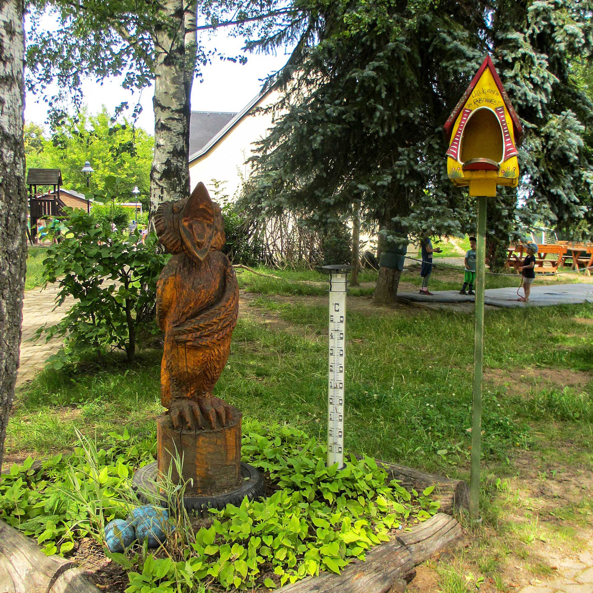Der Eingangsbereich zum Garten mit einem Vogelhaus, einer Wetterstation und Holzfigur.