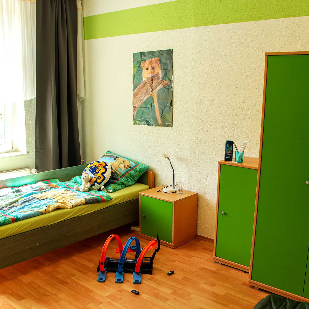 Ein Kinderzimmer mit einem Bett, Schrank und Nachttischschrank.