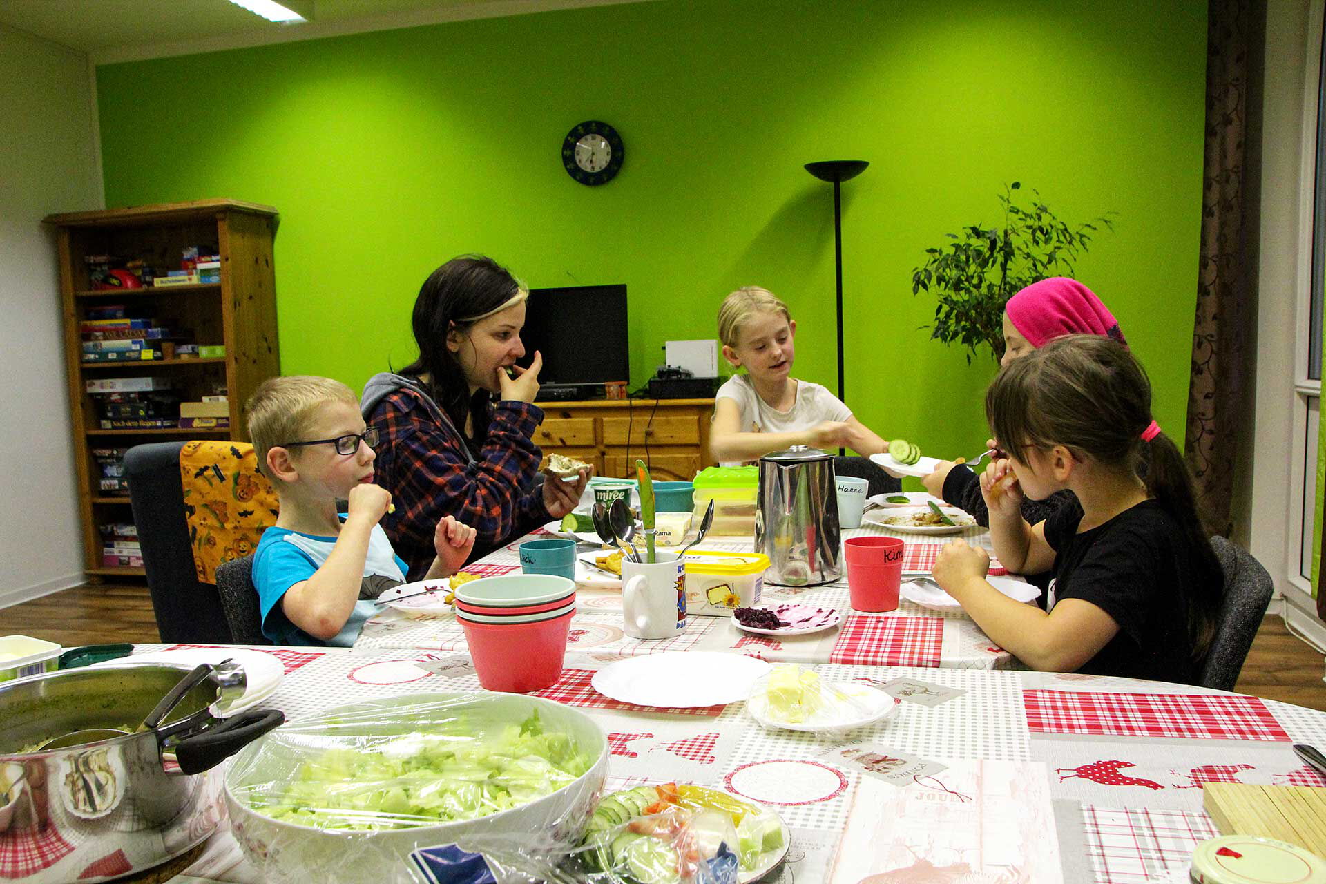 An einem großen Esstisch sitzen fünf Kinder und essen zu Abend. Auf dem Tisch stehen Teller, Schüsseln und es gibt Salat und Suppe.