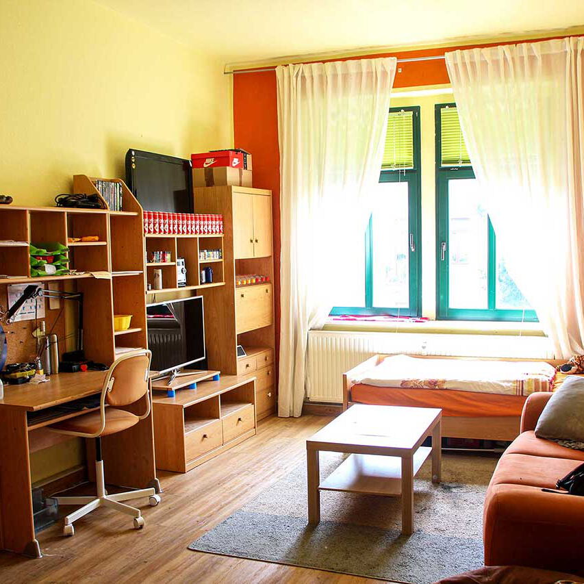 Ein großes Jugendzimmer mit einer Anbauwand, einem Sofa, Bett und TV. In der Anbauwand ist ein Schreibtisch integriert.