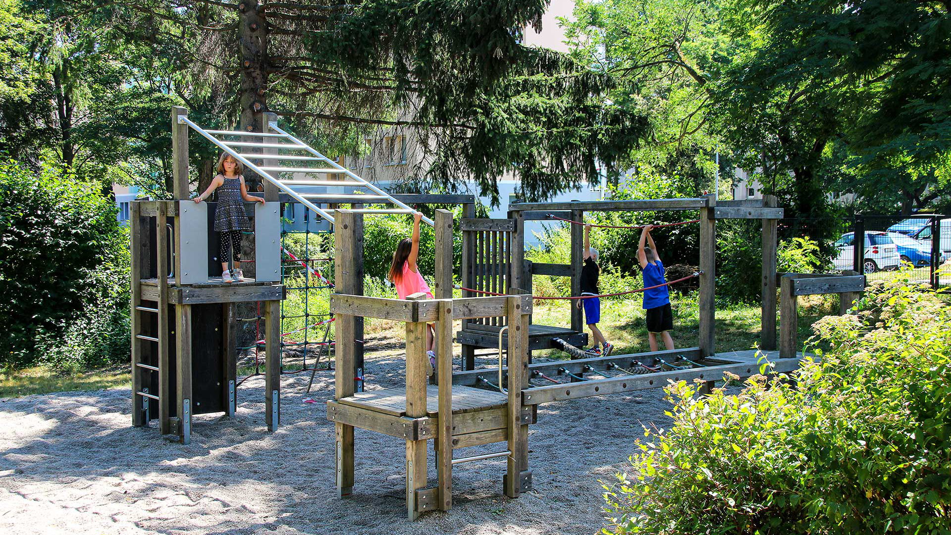 Im Gartenbereich steht ein Klettergüst aus Holz. Es spielen und klettern vier Kind auf dem Klettergerüst.