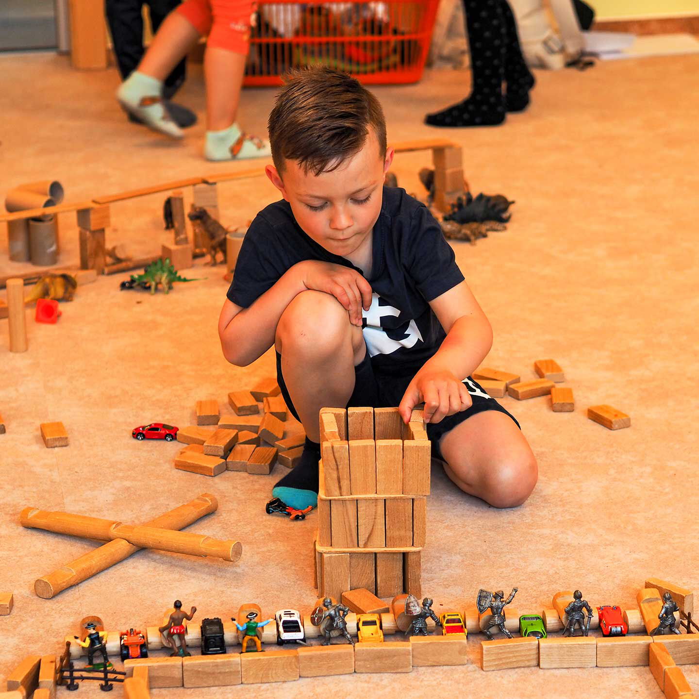 Ein Kind hat im Bauzimmer aus Holzbausteinen einen Turm gebaut. Im Vordergrund stehen verschiedenen Spielfiguren aufgereiht nebeneinander.