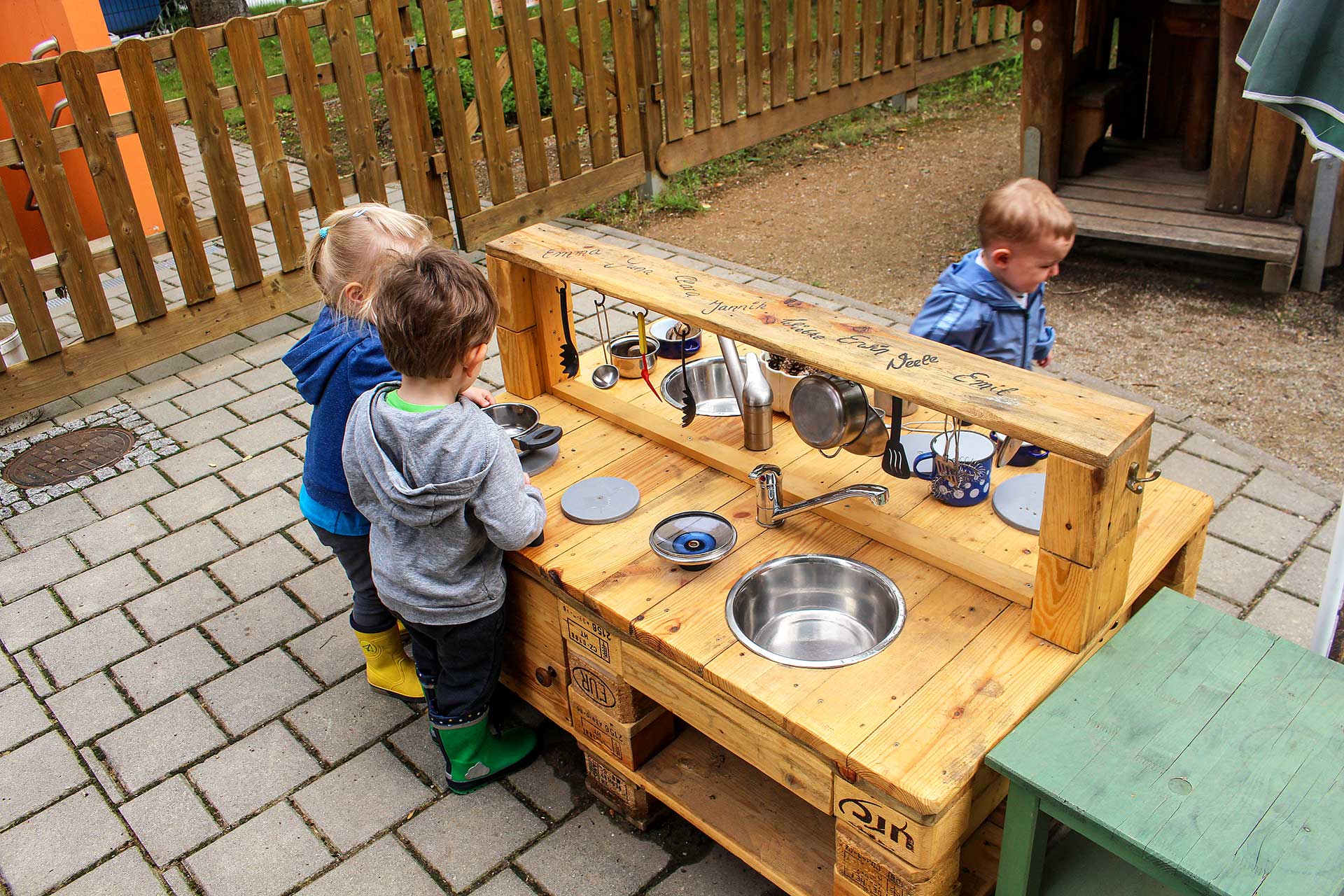 Die selbstgebaute Outdoor Spielküche aus Holzpaletten wird von drei Kindern bespielt.